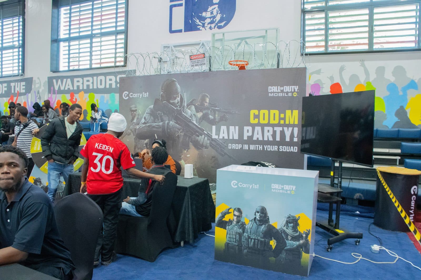 A Call of Duty: Mobile LAN party stand reading Drop in with your squad, players gathered around it in the hall