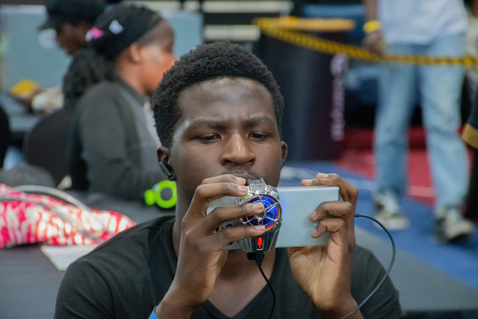 A competitor mid-match, concentrating on a phone fitted with a controller grip, earbuds in