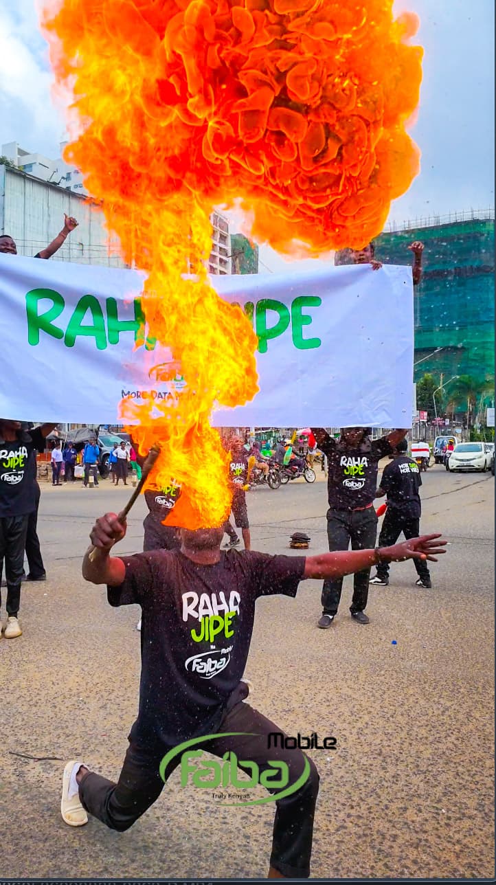 A fire breather blowing a plume of flame in front of the Raha Jipe banner as the crowd watches