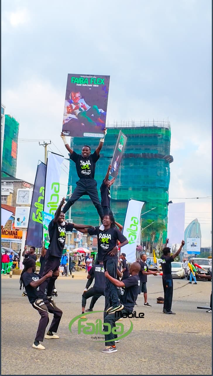 Acrobats in a human pyramid, the topmost holding a Faiba Flex poster above the street