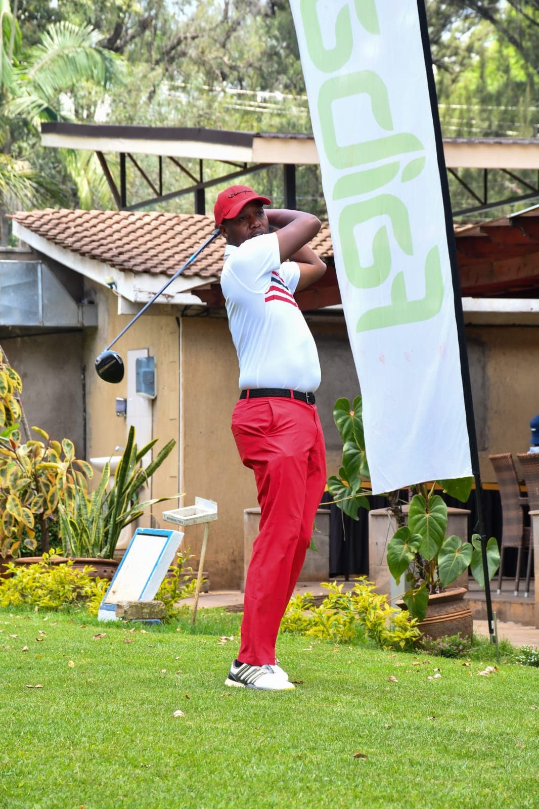A golfer in red driving off beside a Faiba Giga feather flag at the clubhouse
